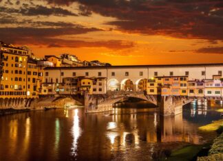 The Ponte Vecchio bridge glows warmly over the Arno River at sunset with vibrant skies, 4K Desktop Wallpaper