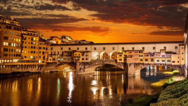 The Ponte Vecchio bridge glows warmly over the Arno River at sunset with vibrant skies, 4K Desktop Wallpaper