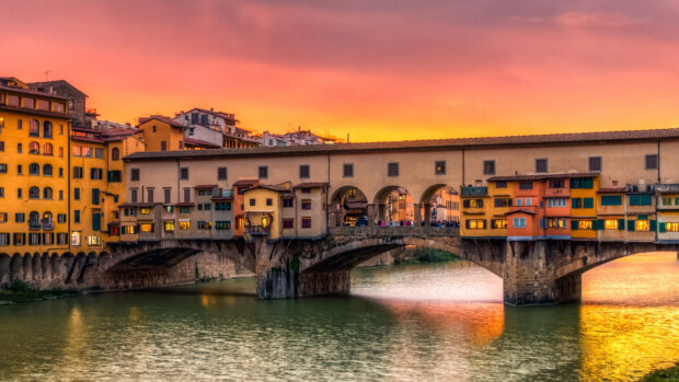 The historic Ponte Vecchio is shown with vibrant sunset colors reflecting on the river, HD Desktop Wallpaper