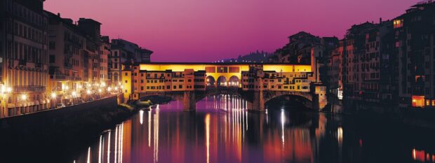 The Ponte Vecchio reflects beautifully in the calm river during sunset with vibrant colors, 2K Desktop Wallpaper