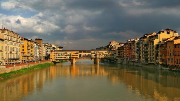 The sunset reflects warmly on the Ponte Vecchio and surrounding buildings in Florence, 4K Desktop Wallpaper