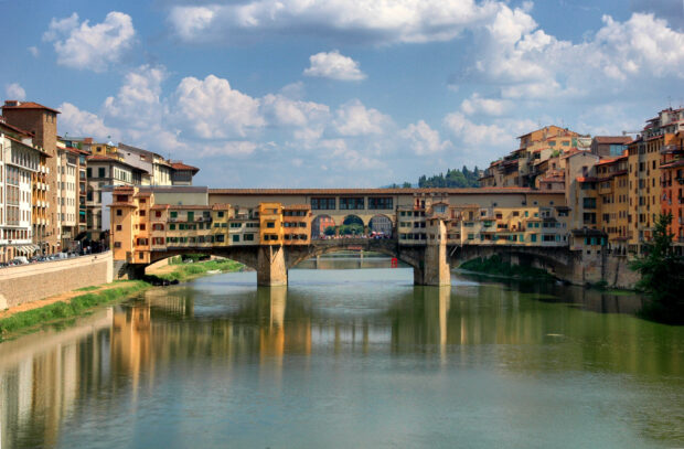The Ponte Vecchio is seen over the Arno river under a blue sky, 2K Desktop Wallpaper