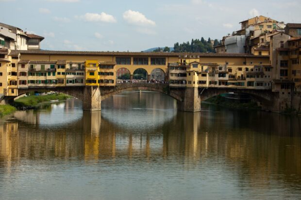 The Ponte Vecchio spans a calm river with its historic buildings reflecting on the water, 2K Desktop Wallpaper