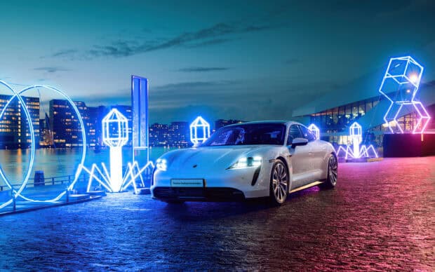 A Porsche Taycan is parked near illuminated city sculptures at dusk, 2K Desktop Wallpaper