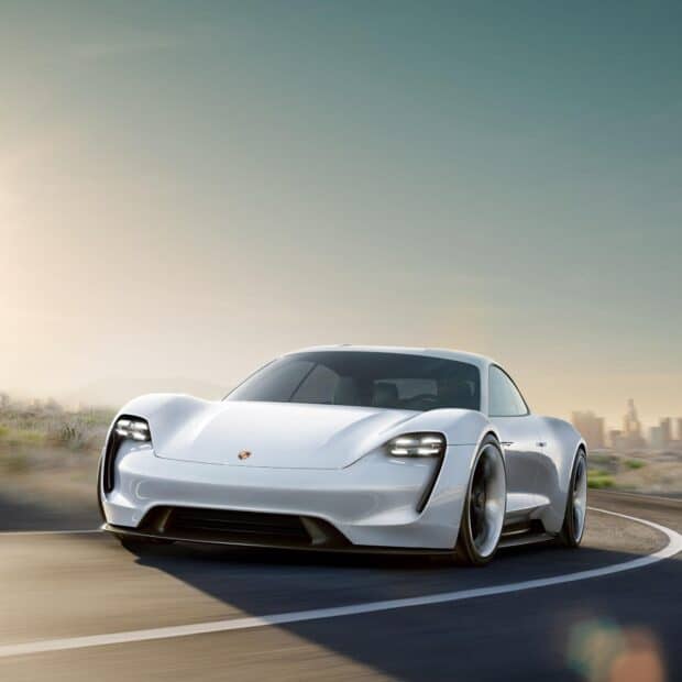 A white Porsche Taycan is driving smoothly on a curved road with a city skyline in the background during sunset, HD Desktop Wallpaper