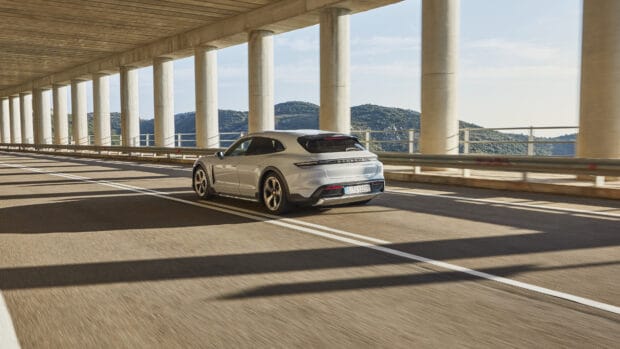 A silver Porsche Taycan is driving under a bridge with pillars on a sunny day, 4K Desktop Wallpaper