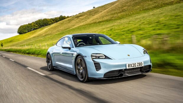 A Porsche Taycan is driving fast on a countryside road with green hills in the background, 2K Desktop Wallpaper