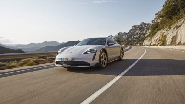 A Porsche Taycan drives along a curved mountain road under a clear sky, 2K Desktop Wallpaper