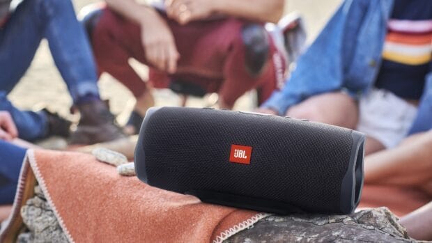 A portable JBL speaker is placed on a log with people relaxing in the background, HD Desktop Wallpaper