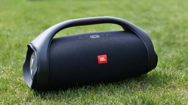 A portable JBL speaker is shown resting on green grass outdoors, 2K Desktop Wallpaper