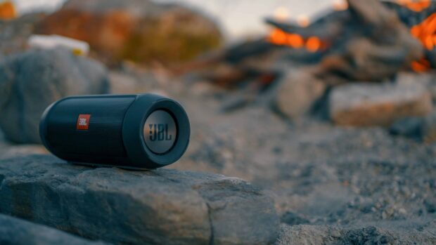 A portable JBL speaker is placed on rocks near a campfire outdoors, 2K Desktop Wallpaper