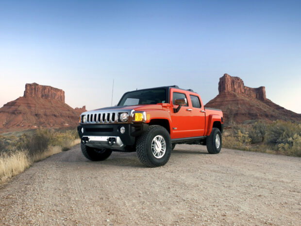 A bright orange Hummer H3 drives on a dirt road with rocky formations in the background, HD Desktop Wallpaper