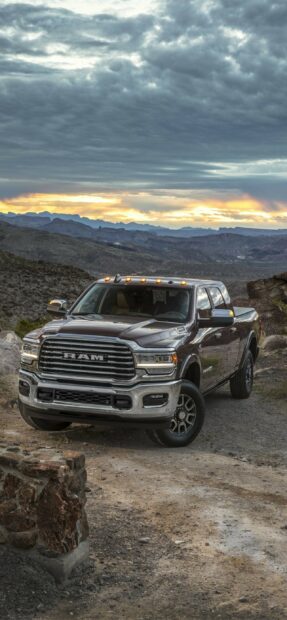 A Ram pickup truck is parked on a dirt road with mountains and a dramatic cloudy sky in the background, 2K Mobile Wallpaper