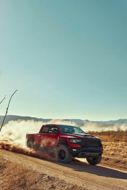 A red Ram truck is kicking up dust while driving fast on a desert road with mountains in the background, HD Mobile Wallpaper
