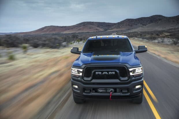 A powerful Ram truck is driving down a two lane road with mountains in the background, 2K Desktop Wallpaper