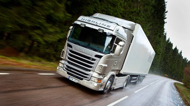 A white Scania truck drives swiftly on a rainy forest road showing strength and speed, 4K Desktop Wallpaper