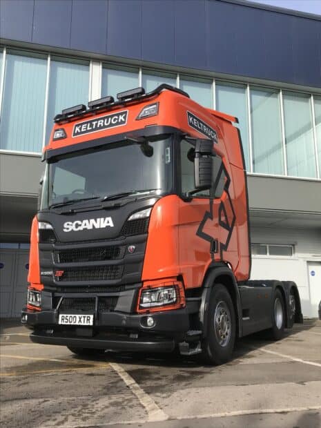 A bright orange Scania truck is parked outside a building with blue glass windows, HD Desktop Wallpaper