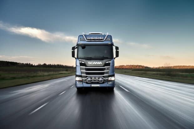 A powerful Scania truck is driving fast on a wet highway with a clear sky, 2K Desktop Wallpaper