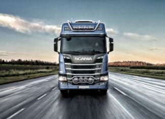 A Scania truck drives forward on a wet highway under a cloudy sky, 2K Desktop Wallpaper