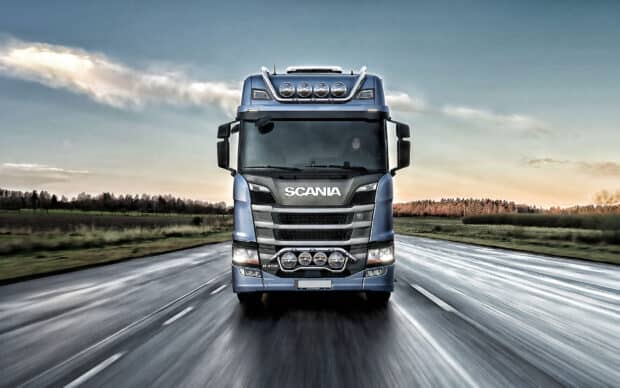 A Scania truck drives forward on a wet highway under a cloudy sky, 2K Desktop Wallpaper