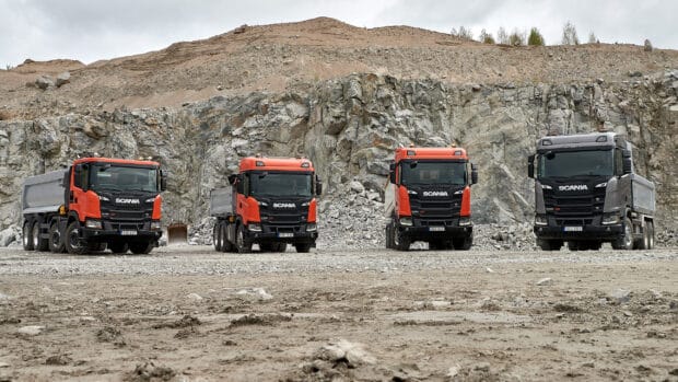 Four Scania trucks standing in front of rocky hills showcasing strength and durability, 2K Desktop Wallpaper