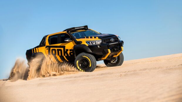 A yellow and black truck performs off road driving on sand dunes in the desert, 2K Desktop Wallpaper