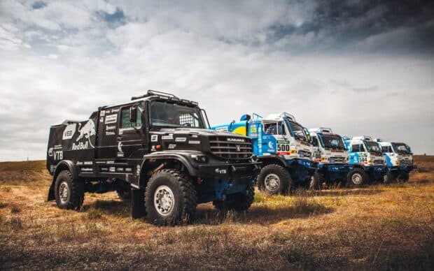 Rally raid trucks stand ready for off road racing in open field, 2K Desktop Wallpaper
