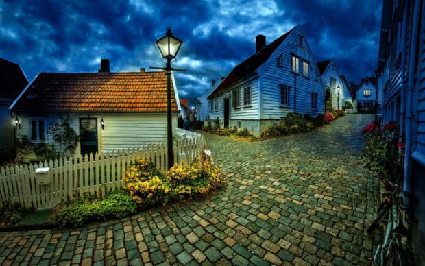 A peaceful village street with cobblestone pavement and traditional houses under a cloudy evening sky, HD Desktop Wallpaper