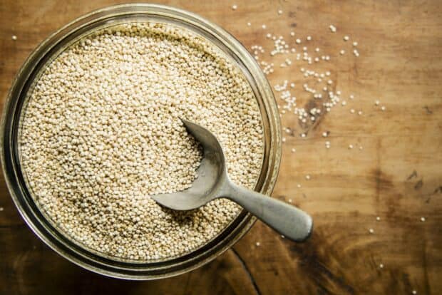 A metal spoon resting in a jar filled with quinoa grains on a wooden surface, HD Desktop Wallpaper