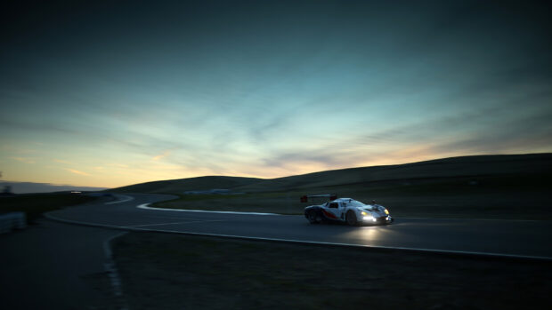 A race car is driving fast on a race track under a darkening sky, HD Desktop Wallpaper