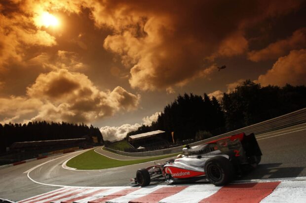 A race car is taking a sharp turn on the race track under dramatic cloudy skies during sunset, HD Desktop Wallpaper