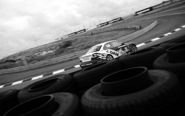 A race car is seen speeding on a curved track surrounded by tire barriers in black and white, HD Desktop Wallpaper
