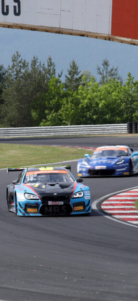 Two race cars compete closely while turning on a curved race track surrounded by trees, 2K Mobile Wallpaper