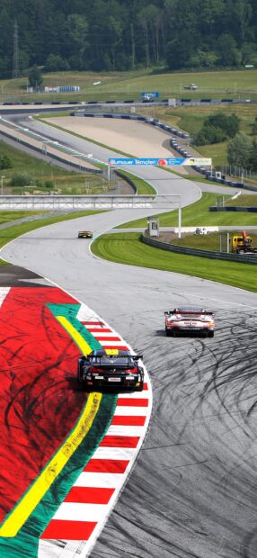 Race cars are speeding around a colorful curving race track in a green landscape, 2K Phone Wallpaper