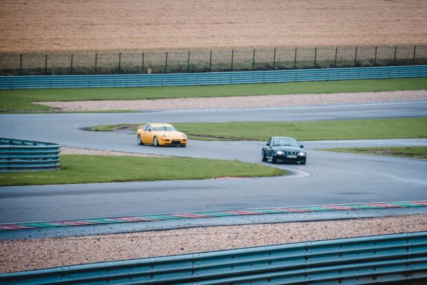 Two cars racing on a sharp race track curve in an open field, 2K Desktop Wallpaper