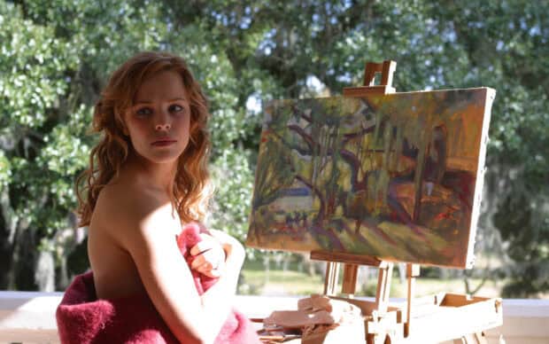 Rachel Mcadams is sitting beside an easel with a painting in a sunlit environment, 2K Desktop Wallpaper