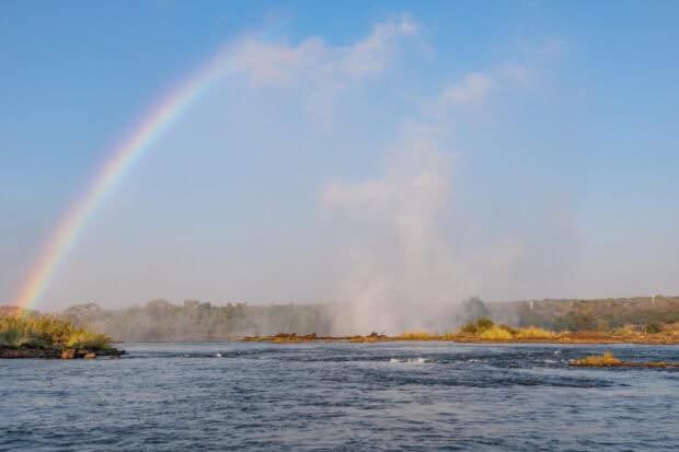 A rainbow appears over Devils Pool Zambia with mist rising from the water, HD Desktop Wallpaper