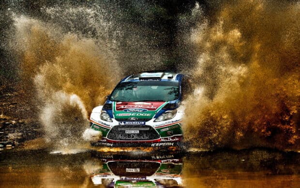 A rally raid race car speeds through muddy water creating a large splash, 2K Desktop Wallpaper