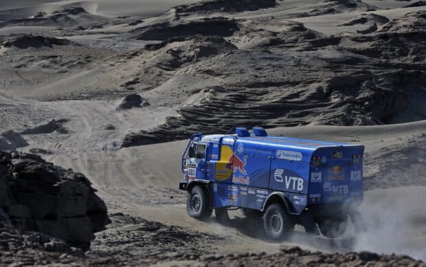 A blue rally raid truck speeds through a rocky desert terrain kicking up dust, HD Desktop Wallpaper