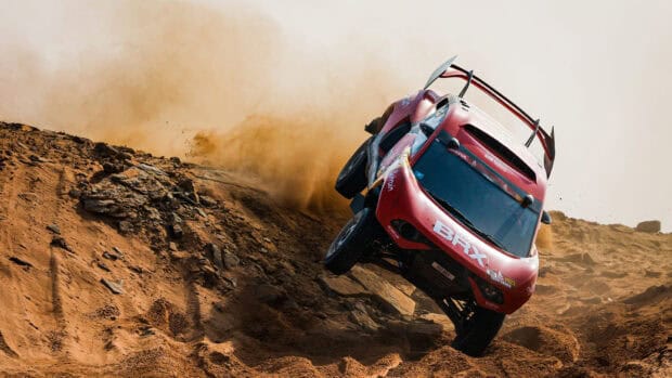 A red rally raid car kicks up dust while racing through a rocky desert terrain, HD Desktop Wallpaper