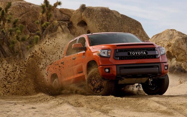 A rally raid vehicle kicks up sand while driving through rocky desert terrain, HD Desktop Wallpaper