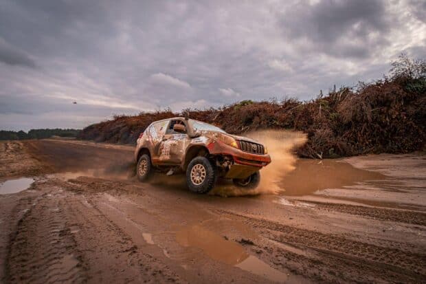 A rally raid vehicle speeds through muddy terrain kicking up dirt and water, HD Desktop Wallpaper