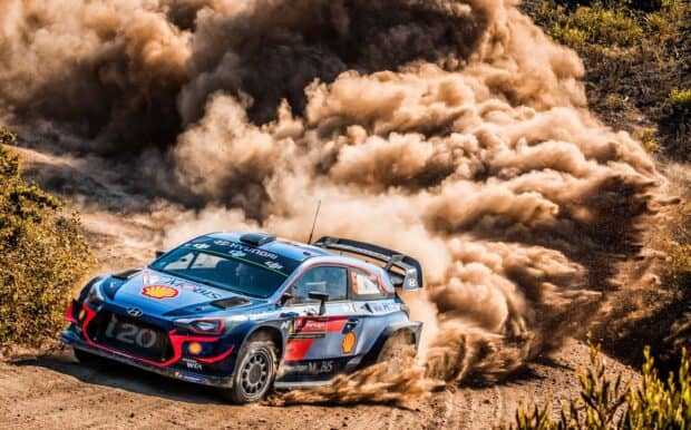 A rally raid car kicks up dust as it speeds through a dirt track surrounded by foliage, 2K Desktop Wallpaper