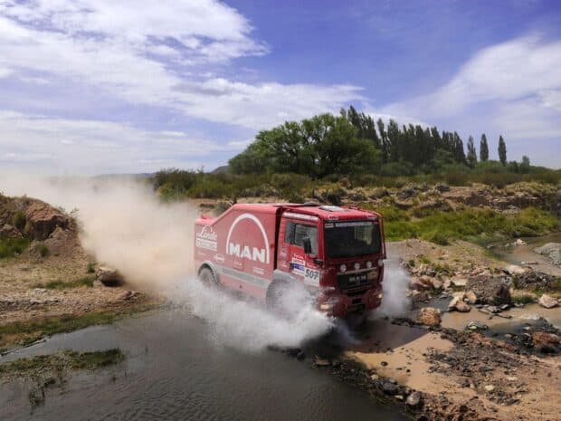 A rally raid truck splashes through a shallow river in a rugged terrain, HD Desktop Wallpaper