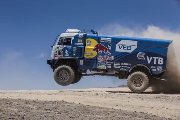 A rally raid truck is airborne over a sandy desert during a race event, 2K Desktop Wallpaper