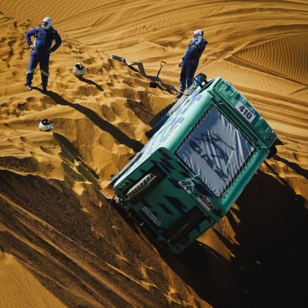 A rally raid truck is stuck in the desert with two men standing nearby, HD Mobile Wallpaper