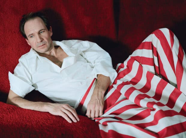 Ralph Fiennes is lying on a red couch wearing a white shirt and striped pants, HD Desktop Wallpaper