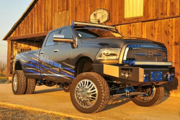 A Ram truck with custom blue stripe design is parked near a wooden barn under warm sunlight, 2K Desktop Wallpaper