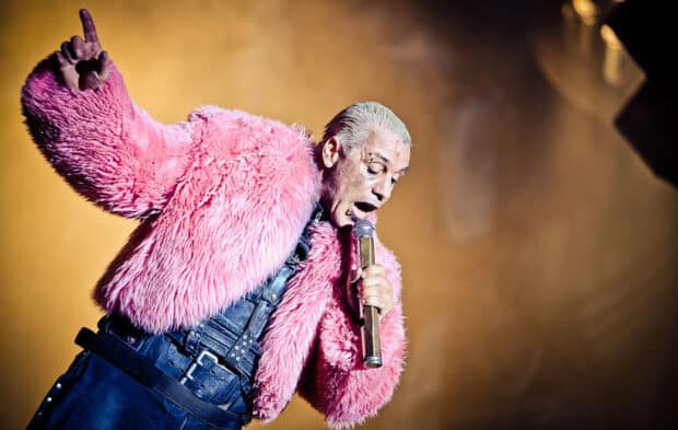 The Rammstein frontman wears a bright pink fur jacket while singing passionately on stage during a live concert, HD Desktop Wallpaper