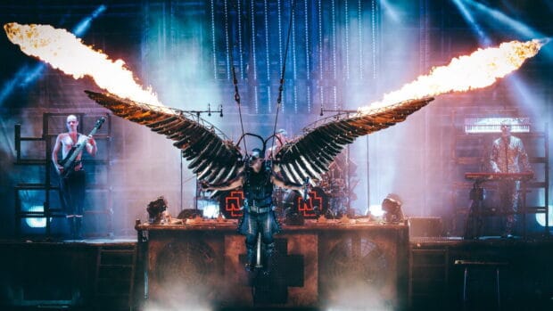 A Rammstein band member performs with large mechanical wings and flames on stage, 4K Desktop Wallpaper